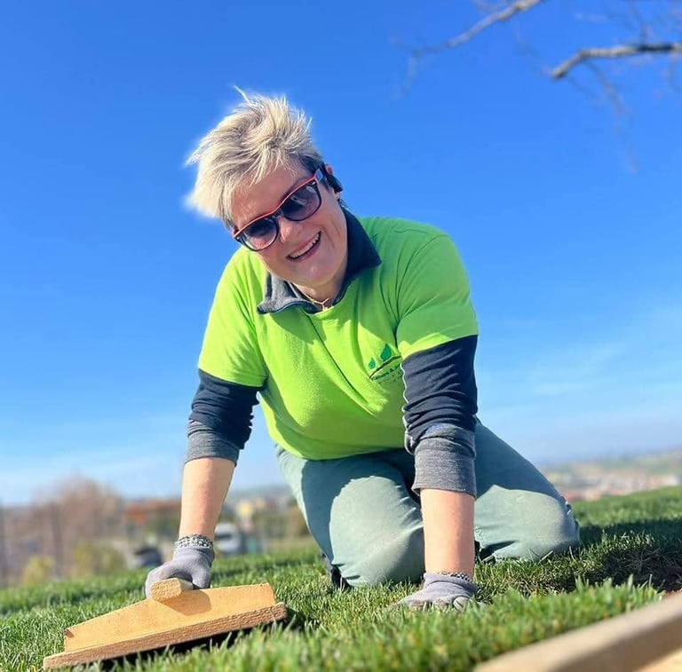 Person in neon green shirt and sunglasses crouching outdoors on grass with cornhole board