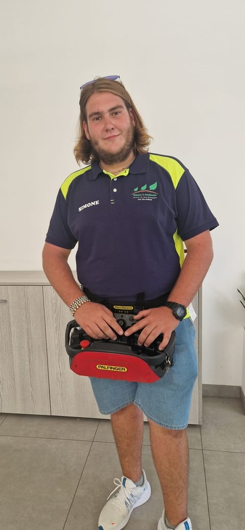 Man with shoulder-length brown hair wearing navy polo shirt with neon yellow accents holding a red toolbox, standing against white background