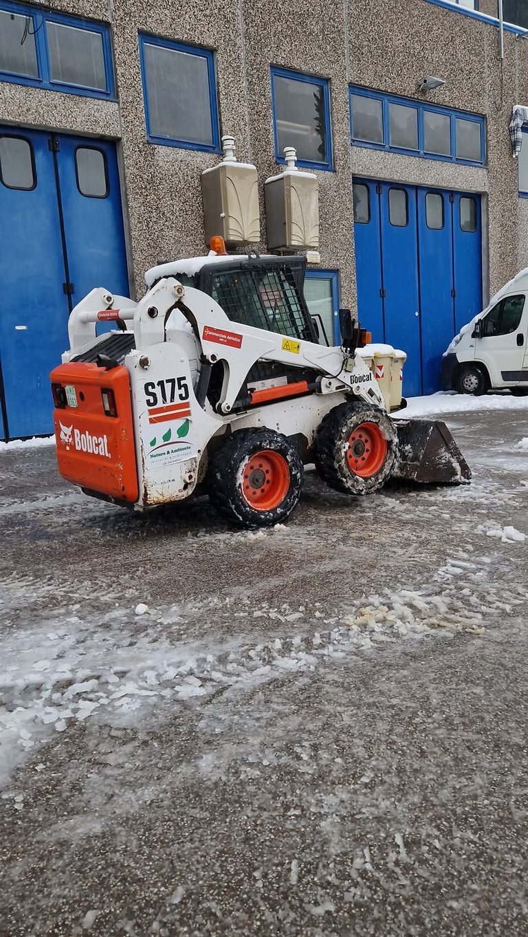A Bobcat S175 skid steer loader parked in front of a blue industrial building with snow on the ground