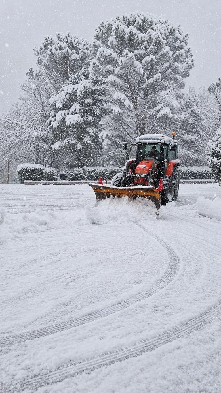 Spazzaneve rosso che pulisce una strada innevata durante una forte nevicata